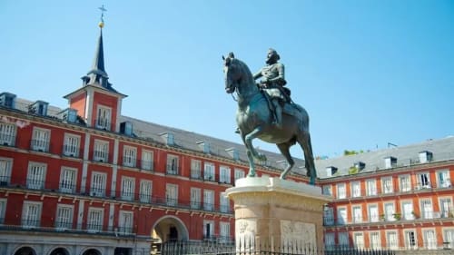 Equestrian statue on Plaza Mayor in Madrid with red historic buildings and church bell tower backdrop