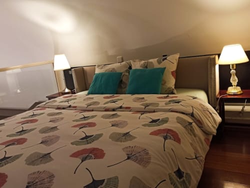 Elegant bedroom with patterned bedding, teal pillows, upholstered headboard, bedside lamps, and wooden flooring at Charming