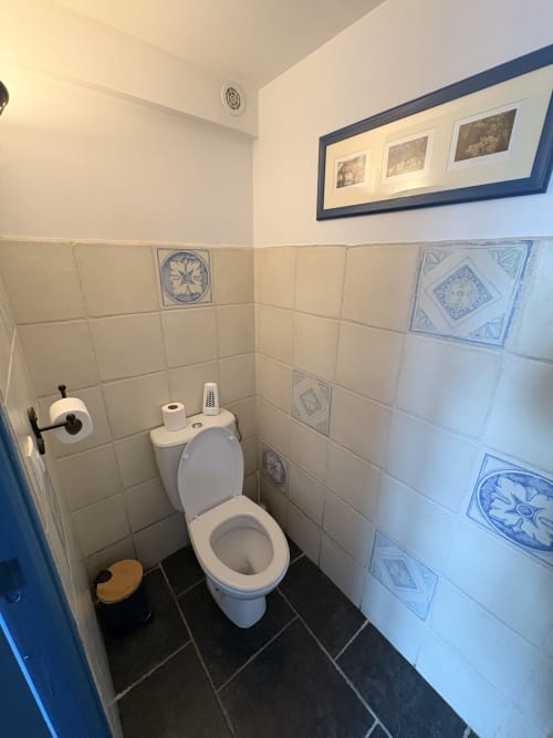 Compact toilet room with cream and blue decorative tiles, paper holder, and dark flooring at Ferme de la Forterie Verlinghem,