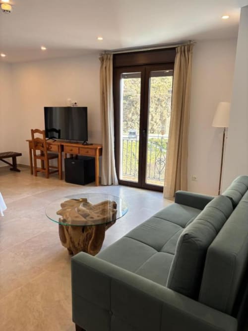 Modern living room at Hotel Mulhacén Trevélez with gray sofa, TV desk, and balcony overlooking Granada mountains