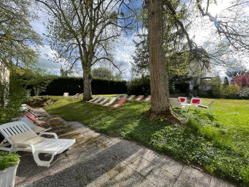Jardin de l'Hôtel d'Angleterre avec transats, grands arbres et pelouse soignée à Vittel