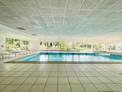 Piscine intérieure de l'Hôtel d'Angleterre à Vittel avec eau bleue, grandes baies vitrées et plafond moderne