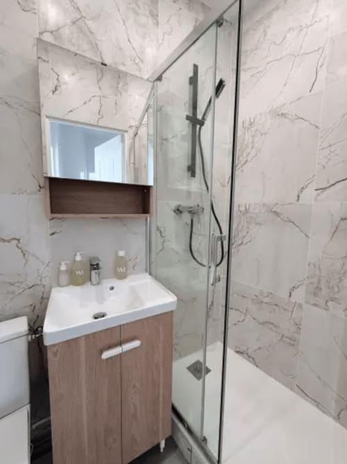 Salle de bain moderne de l'appartement ARLOÉ avec carrelage marbre, meuble vasque en bois, lavabo blanc et douche à l'italienne, La Rochelle