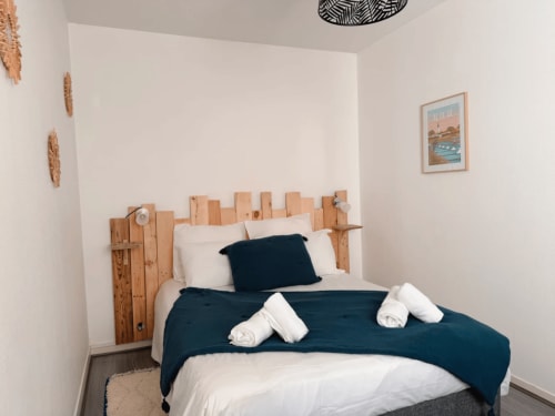 Chambre cosy de l'appartement ARLOÉ à La Rochelle avec tête de lit bois, literie bleu marine et serviettes blanches