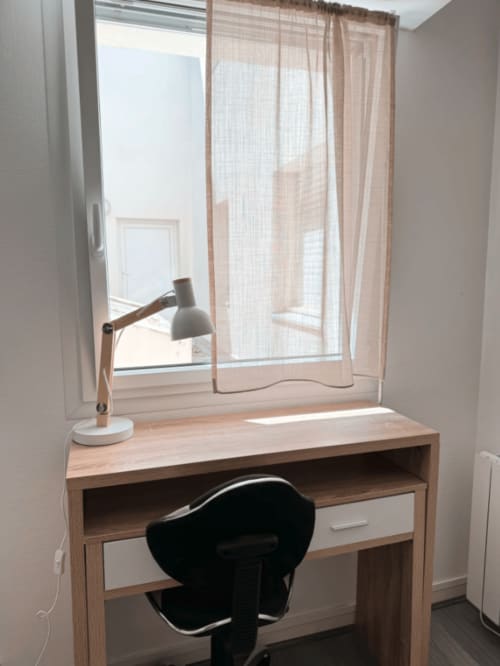 Espace de travail lumineux à l'appartement ARLOÉ La Rochelle avec bureau en bois, chaise noire, lampe de bureau et vue sur la ville par la fenêtre