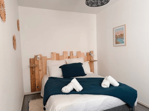 Chambre moderne de l'appartement ARLOÉ à La Rochelle avec tête de lit en bois, literie bleu marine et oreillers blancs