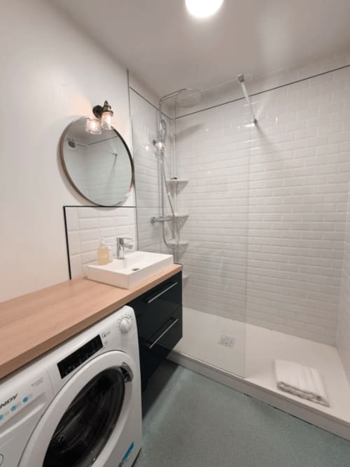 Salle de bain moderne de l'appartement ARLOÉ à La Rochelle avec carrelage métro blanc, miroir rond, vasque et douche spacieuse