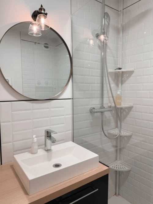 Salle de bains moderne de l'appartement ARLOÉ à La Rochelle avec miroir circulaire, carrelage blanc et douche vitrée