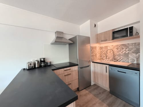 Cuisine moderne de l'appartement ARLOÉ à La Rochelle avec plan de travail noir, meubles en bois et électroménagers inox