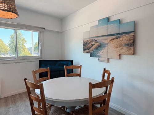 Salle à manger moderne de l'appartement ARLOÉ à La Rochelle avec table ronde, chaises en bois, œuvres marines et vue sur la ville