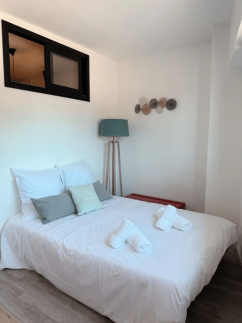 Chambre moderne de l'appartement ARLOÉ à La Rochelle avec literie blanche, lampe turquoise et décoration murale minimaliste