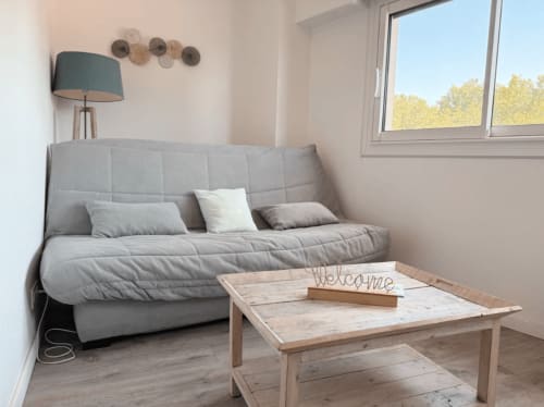 Séjour cosy de l'appartement ARLOÉ La Rochelle avec canapé gris, table en bois et vue sur la ville