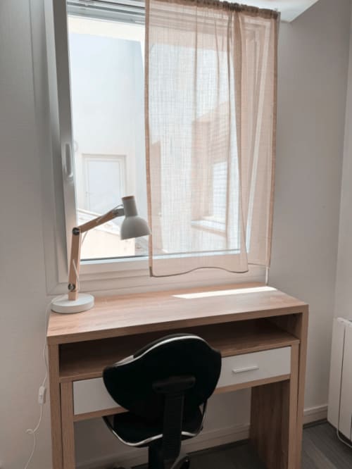 Espace de travail lumineux à ARLOÉ, appartement à La Rochelle avec bureau en bois, lampe ajustable et vue sur la ville par la fenêtre