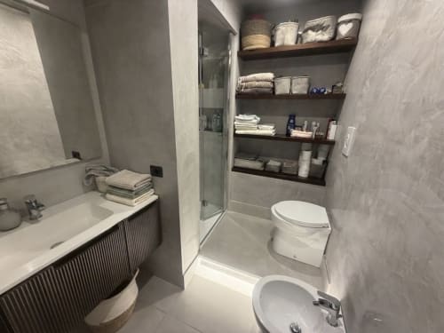 Bagno moderno dell'ROOMITO APARTMENTS Napoli con toilette bianca, lavandino, box doccia e ripiani in legno scuro