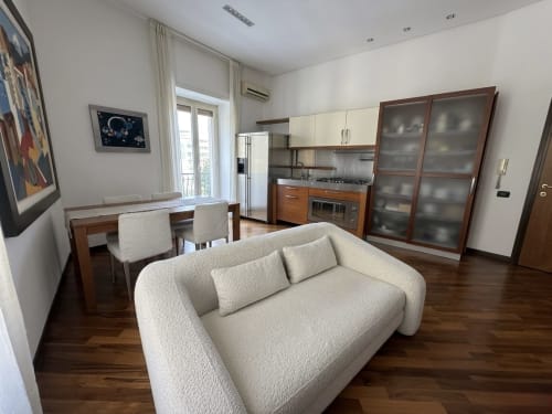 Moderna zona giorno open-plan presso ROOMITO APARTMENTS Napoli con divano color crema, zona pranzo, cucina e vista sulla città dal balcone