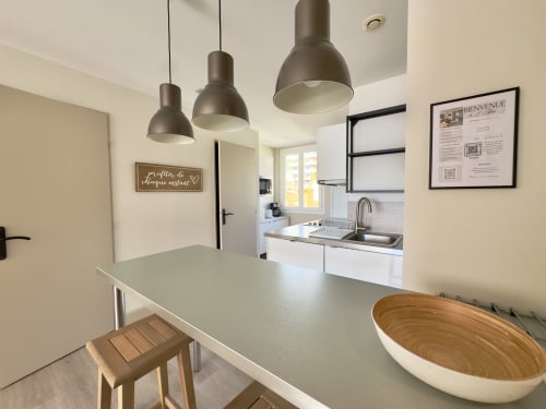 Cuisine-salle à manger moderne de l'appartement SoleMare avec luminaires suspendus, plan de travail blanc et accessoires en bois
