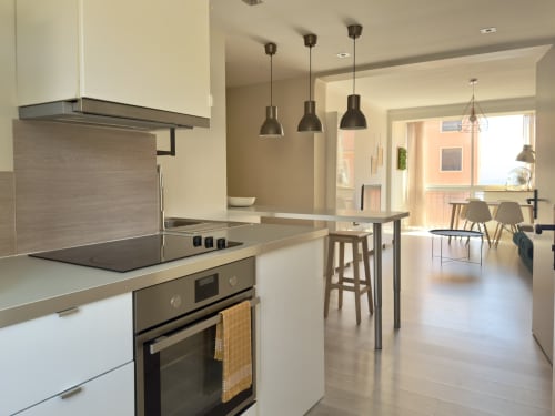 Cuisine moderne avec électroménagers en inox, armoires blanches et luminaires suspendus noirs, appartement L'Ajax, Alata