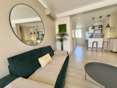 Séjour spacieux et lumineux avec canapé vert, miroir rond et cuisine ouverte à Alata, Corse
