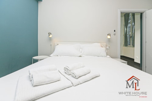 Camera da letto moderna alla ML White House di Genova con biancheria bianca, parete azzurra e vista sulla città