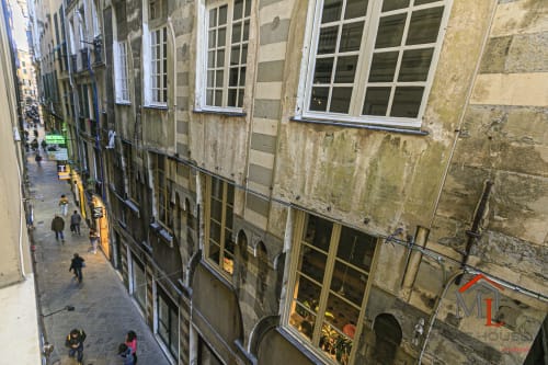 Vicolo storico di Genova con edifici in pietra, finestre e pedoni nel Centro Storico