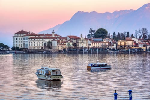 Pittoresco borgo lacustre con edifici variopinti fronte acqua, barche e montagne al tramonto presso MiSaNi Apartments