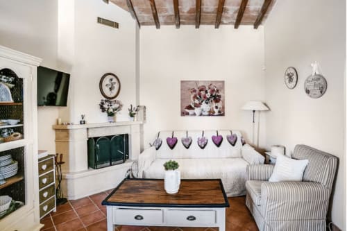 Cozy living room at Casa Rossi Roma with fireplace, white sofa, striped armchair, and rustic wood ceiling beams