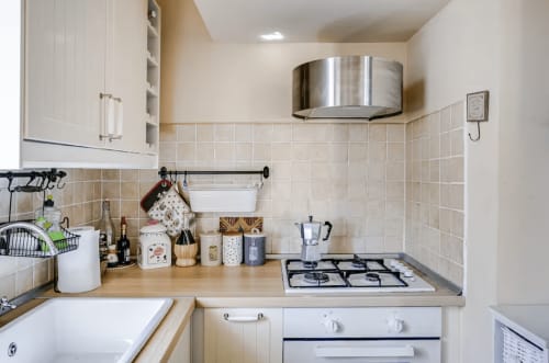 Modern kitchen at Casa Rossi Roma with cream tile backsplash, gas stovetop, stainless steel range hood, and wooden