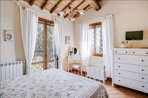 Bright bedroom at Casa Rossi Roma with white furniture, wooden beams, terracotta floors and French doors