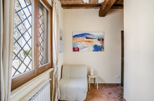 Cozy bedroom at Casa Rossi Roma with wooden beams, sea-themed artwork, terracotta tiles, and latticed windows overlooking