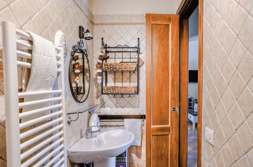 Elegant bathroom at Casa Rossi Roma with white tilework, wicker storage shelves, and wooden door