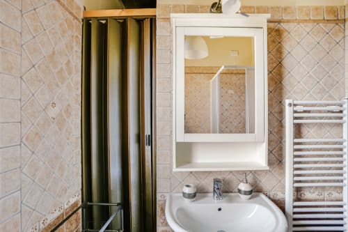 Elegant bathroom at Casa Rossi Roma with beige diamond tile walls, white sink, mirror cabinet, and heated towel rack