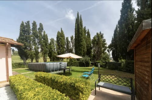 Casa Rossi Roma garden with pool, lounge chairs, cypress trees, and umbrella in Tuscany countryside