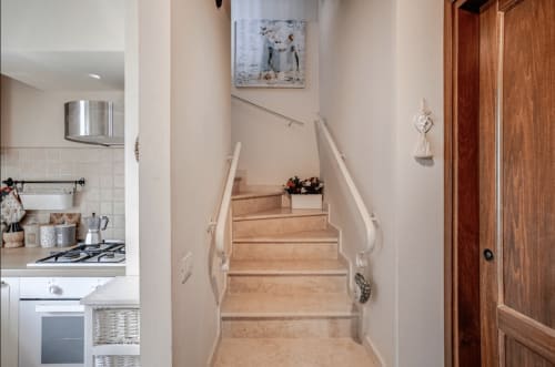 Staircase with wooden steps and white railings at Casa Rossi Roma, leading upstairs with kitchen visible on left