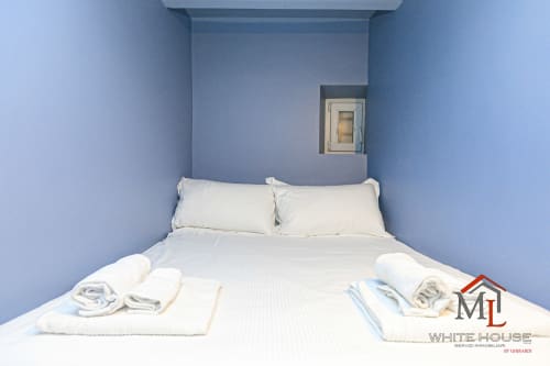 Camera da letto luminosa con pareti blu, biancheria bianca e asciugamani arrotolati presso ML White House apartments nel Centro Storico di Genova