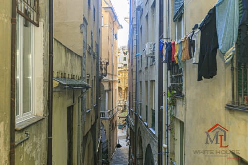 Vicolo stretto nel centro storico di Genova con bucato colorato appeso tra antichi edifici, appartamenti ML White House