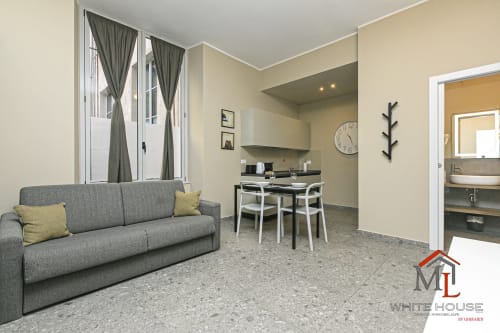 Elegante soggiorno moderno con divano grigio, tavolo da pranzo e angolo cottura nel Centro Storico di Genova