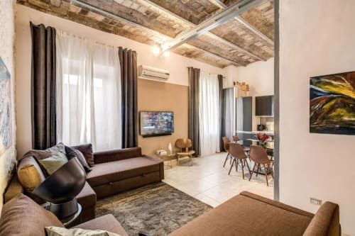 Soggiorno moderno a Roma con divano marrone, TV, zona pranzo e soffitto in mattoni a vista