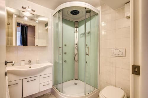 Bagno moderno in appartamento romano con doccia in vetro curvo, lavabo bianco e wc