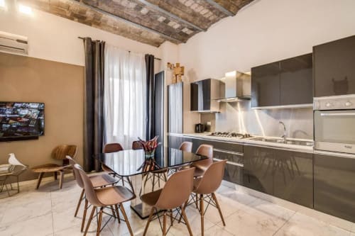 Cucina open-plan moderna e zona pranzo in appartamento del centro di Roma con mobili neri, elettrodomestici in acciaio inox e tavolo da pranzo