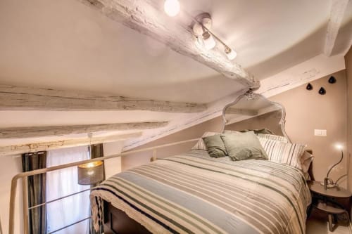 Accogliente camera da letto in soffitta con travi in legno a vista, letto matrimoniale, biancheria a righe e illuminazione calda