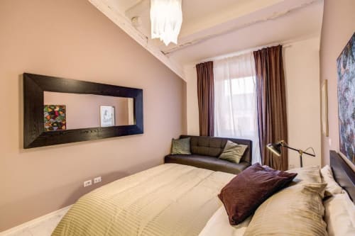 Camera moderna dell'appartamento Downtown Srl Roma con letto queen, divano, specchio e vista sulla corte interna attraverso tende marrone
