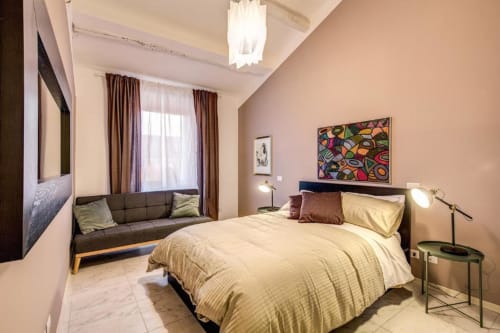 Camera da letto moderna nell'appartamento Downtown Srl Roma con letto matrimoniale, divano grigio, opere d'arte colorate e tende marrone con vista panoramica