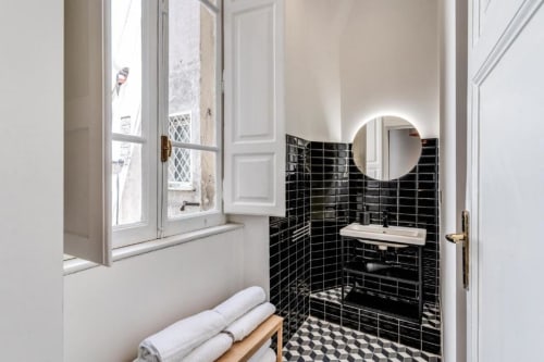 Bagno moderno nell'appartamento di Downtown Roma con piastrelle nere, specchio illuminato rotondo, lavabo bianco e pavimento a scacchi