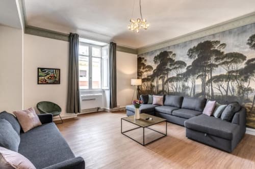 Elegante salotto moderno con divano grigio componibile, carta da parati con vista giardino e arredi contemporanei in appartamento romano