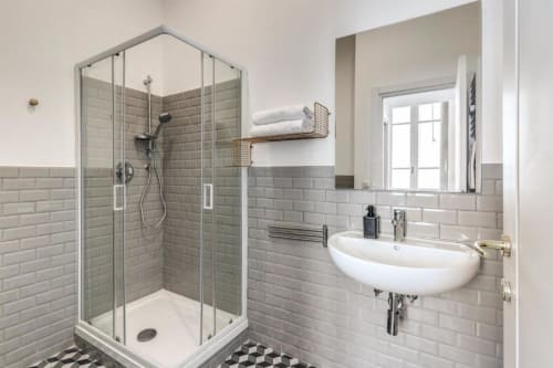 Bagno moderno in appartamento romano con rivestimento doccia in piastrelle grigie, lavabo bianco curvo e piastrelle geometriche nere sul pavimento