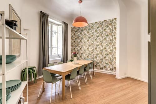 Moderna zona pranzo in appartamento romano con tavolo in legno, sedie verdi, lampada a sospensione corallo e carta da parati con motivi