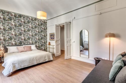 Ampia camera da letto in appartamento romano con carta da parati a fiori, letto matrimoniale, pavimenti in legno, specchio, lampada da terra e zona living