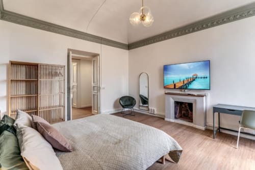 Spaziosa camera da letto romana con letto, TV, camino, specchio, lampada a sospensione moderna e scrivania in legno