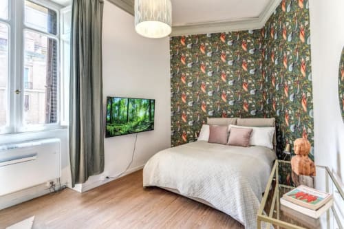 Camera da letto in appartamento moderno a Roma con carta da parati botanica, letto queen size, TV, parquet e finestra con vista giardino
