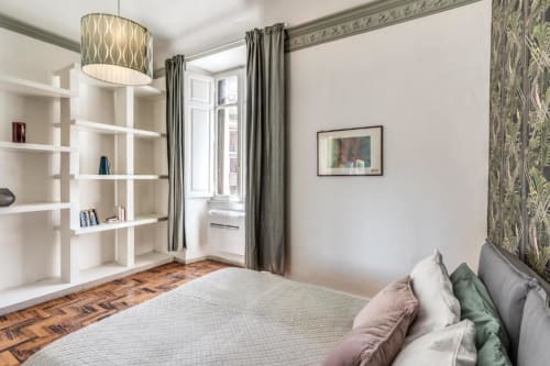 Camera da letto moderna a Roma con letto matrimoniale, mensole bianche, lampadari sospesi e vista sul giardino dalla finestra